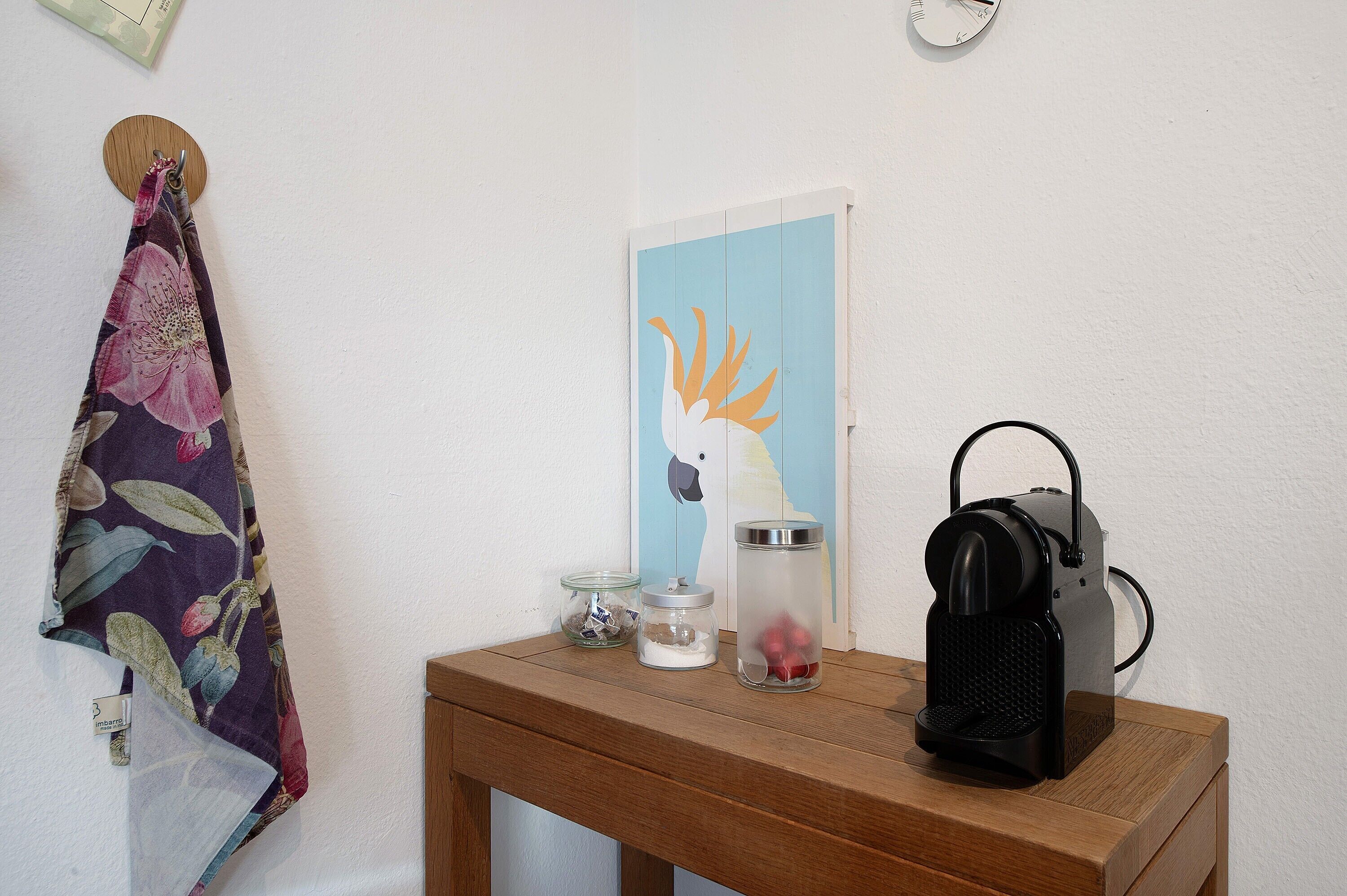 Ein Holztisch mit einer schwarzen Tasche, zwei Glasbehältern und einem an der Wand hängenden Kunstwerk.