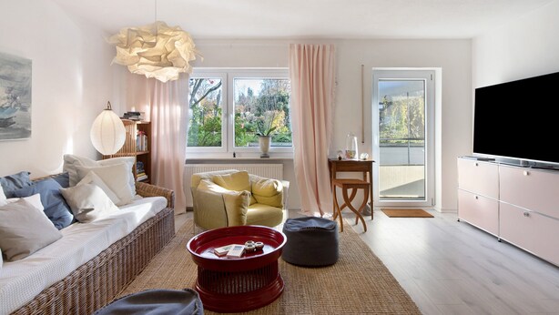 Un salon comprenant un canapé, une table basse rouge, un fauteuil jaune, un téléviseur et une grande fenêtre donnant sur des arbres.