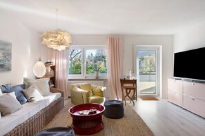 Una sala de estar con un sofá, una mesa de centro roja, un sillón amarillo, un televisor y un ventanal con vistas a árboles.