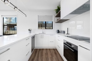 A modern kitchen with white cabinetry, a built-in oven, and a window with a view of a building.