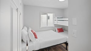 A room with a bunk bed, a single bed, white walls, a window with blinds, and a ceiling light. - Spacious Riverside Suite | Kitchenette, BBQ, Dock (Lake Cowichan)