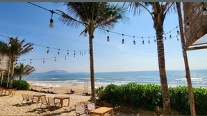 A beachside setting with string lights, palm trees, and beach chairs. - Apec Mandala  View Bien (Hoa Thang)