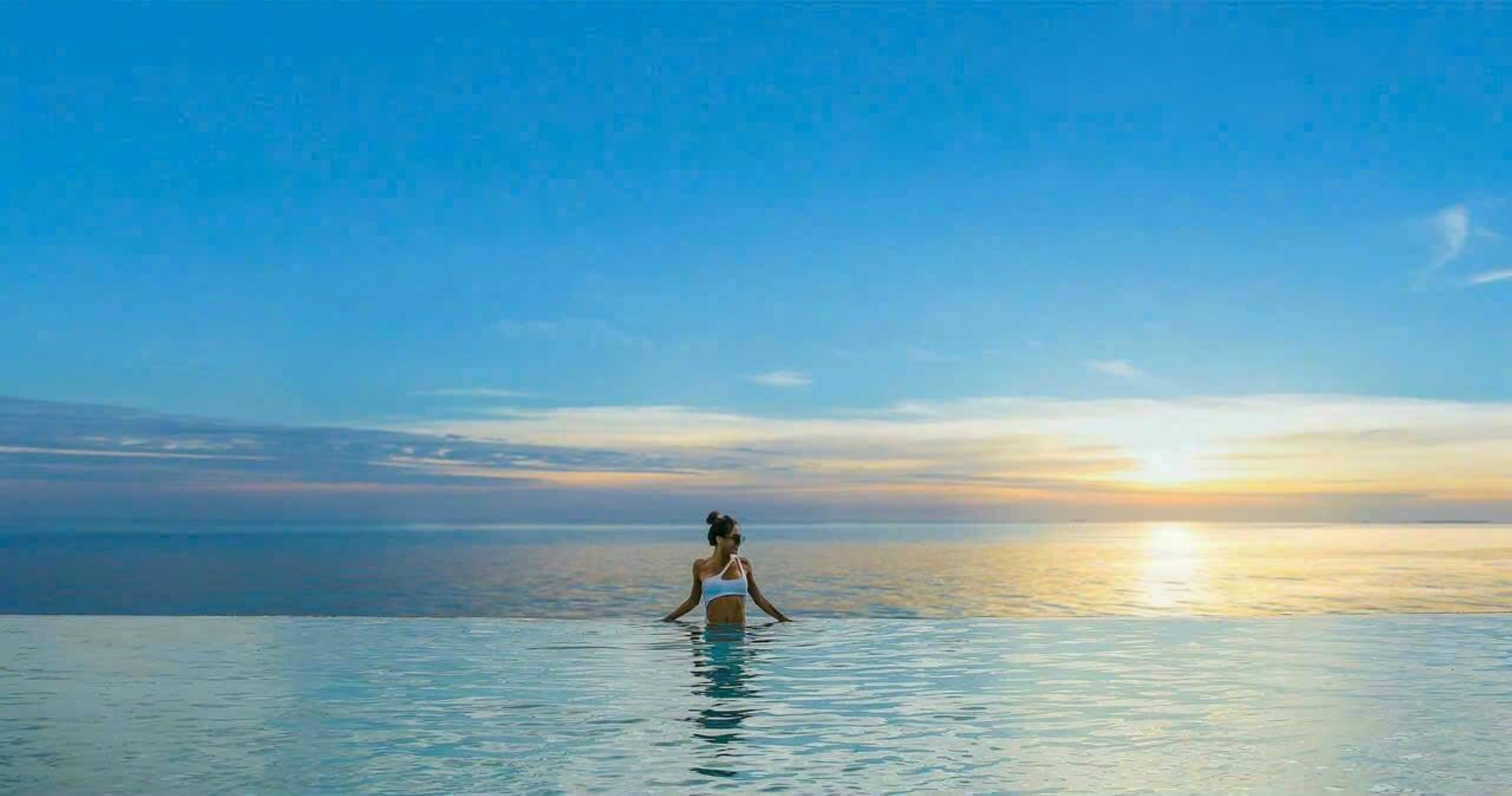 A person standing in a pool with a sunset in the background.