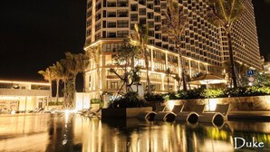 A high-rise hotel with a distinctive geometric facade, a pool area with sun loungers, and palm trees. - Apec Mandala  View Bien (Hoa Thang)