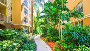 A pathway flanked by lush greenery and yellow buildings with multiple windows and balconies. - Exclusive Yacht Club Condo 10 Min to the Beach (Miami)