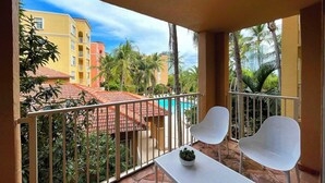 A balcony with white chairs and a table, overlooking a pool and buildings. - Exclusive Yacht Club Condo 10 Min to the Beach (Miami)