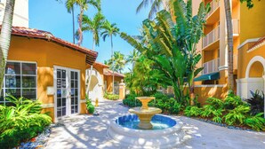 A hotel courtyard with a fountain, palm trees, and a building with a tiled roof. - Exclusive Yacht Club Condo 10 Min to the Beach (Miami)