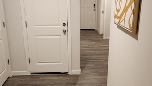 Een gang met houten vloer, witte deuren en een lijstwerkkunstwerk aan de muur.