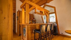 A wooden bar area with four bar stools, a chandelier, and a window with a view.