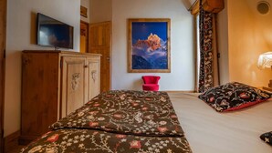 A bedroom with a bed, a wooden wardrobe, a red chair, a painting of a mountain, and a window with curtains.