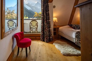 Een slaapkamer met een bed, een rode stoel, een raam met uitzicht op bergen en een houten plafond.