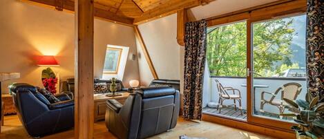 Une pièce chaleureuse avec un plafond en bois, une grande fenêtre avec des rideaux, un canapé en cuir, une petite table avec une lampe et un tapis en peau de vache.