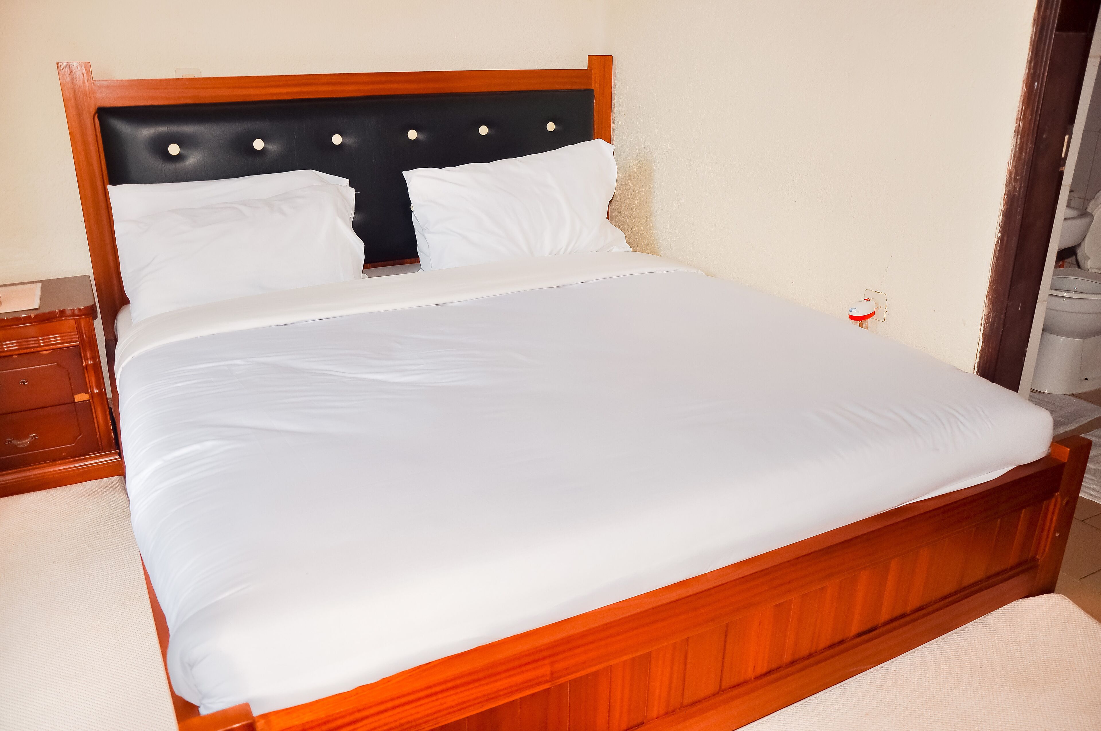 A neatly made bed with white linens, a wooden headboard, and a small bedside table with a lamp.