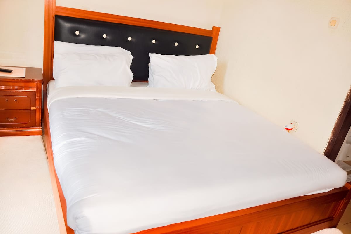 Una cama bien tendida con sábanas blancas, cabecera de madera con detalles circulares y mesita de noche con cajones.