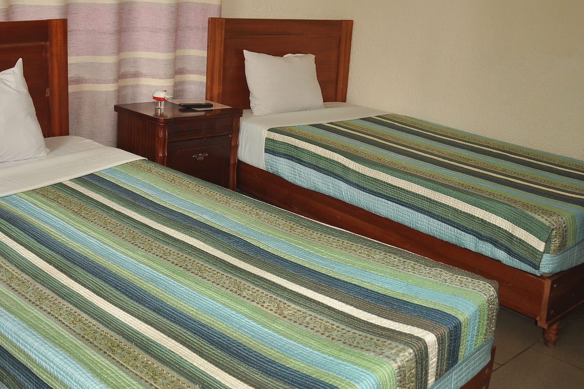 Habitación de hotel con dos camas individuales, cabeceros de madera, una mesita de noche y una mosquitera sobre las camas.