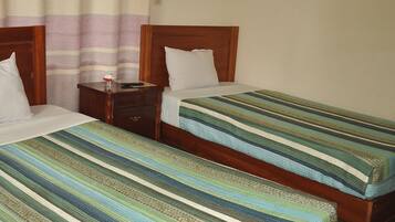 A hotel room with two single beds, wooden headboards, a nightstand, and a mosquito net above the beds.