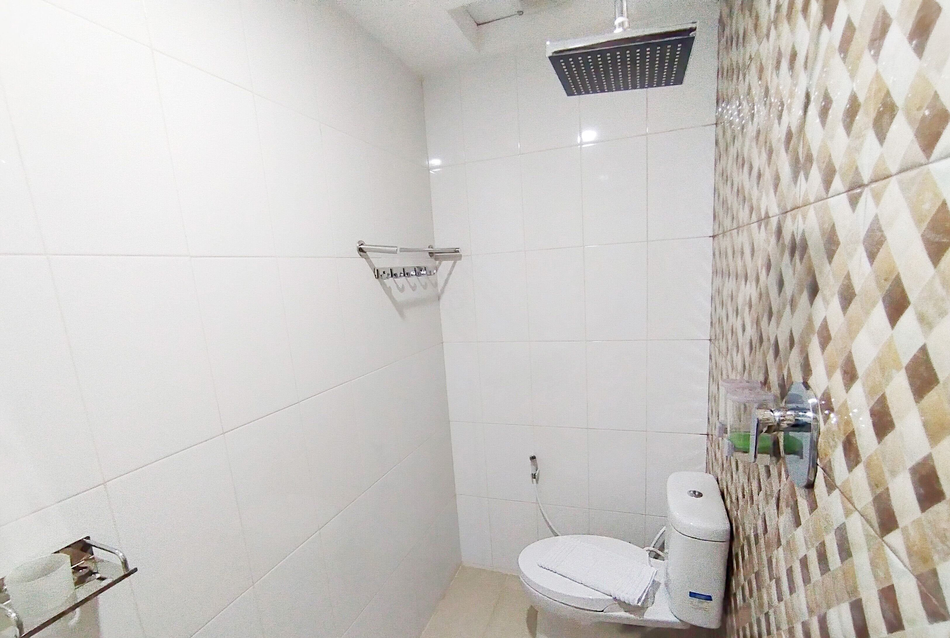 Une petite salle de bain carrelée, équipée d’une douche, de toilettes et d’un porte-serviettes.