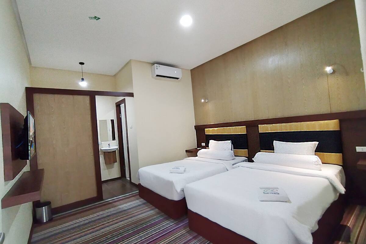 A hotel room with two beds, a TV, a bathroom, and an air conditioning unit.