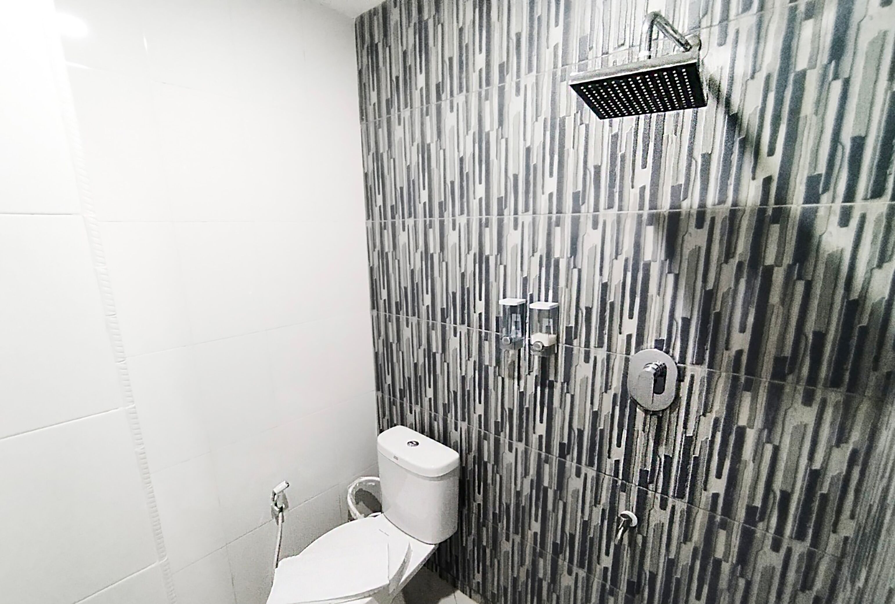 A bathroom with a modern design, featuring a patterned tile wall, a toilet, and a showerhead.