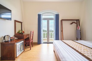 A hotel room with a bed, a desk with a mirror, a chair, a coffee maker, and a view of the outdoors through a glass door. - Dieu Thong Hotel (Xuan Huong - Da Lat)