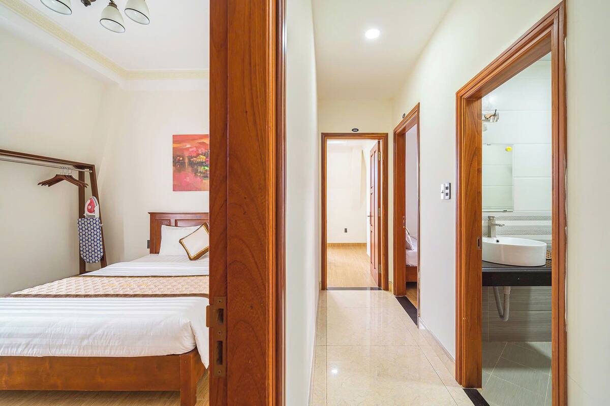 A hotel room with a wooden bed, a bedside table, a hanging coat rack, and a bathroom visible through an open door.