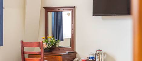 Una habitación de hotel con cama, un escritorio de madera con teléfono, un refrigerador pequeño y un televisor montado en la pared.
