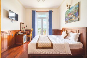 A hotel room with a bed, a desk, a television, and a painting on the wall. - Dieu Thong Hotel (Xuan Huong - Da Lat)