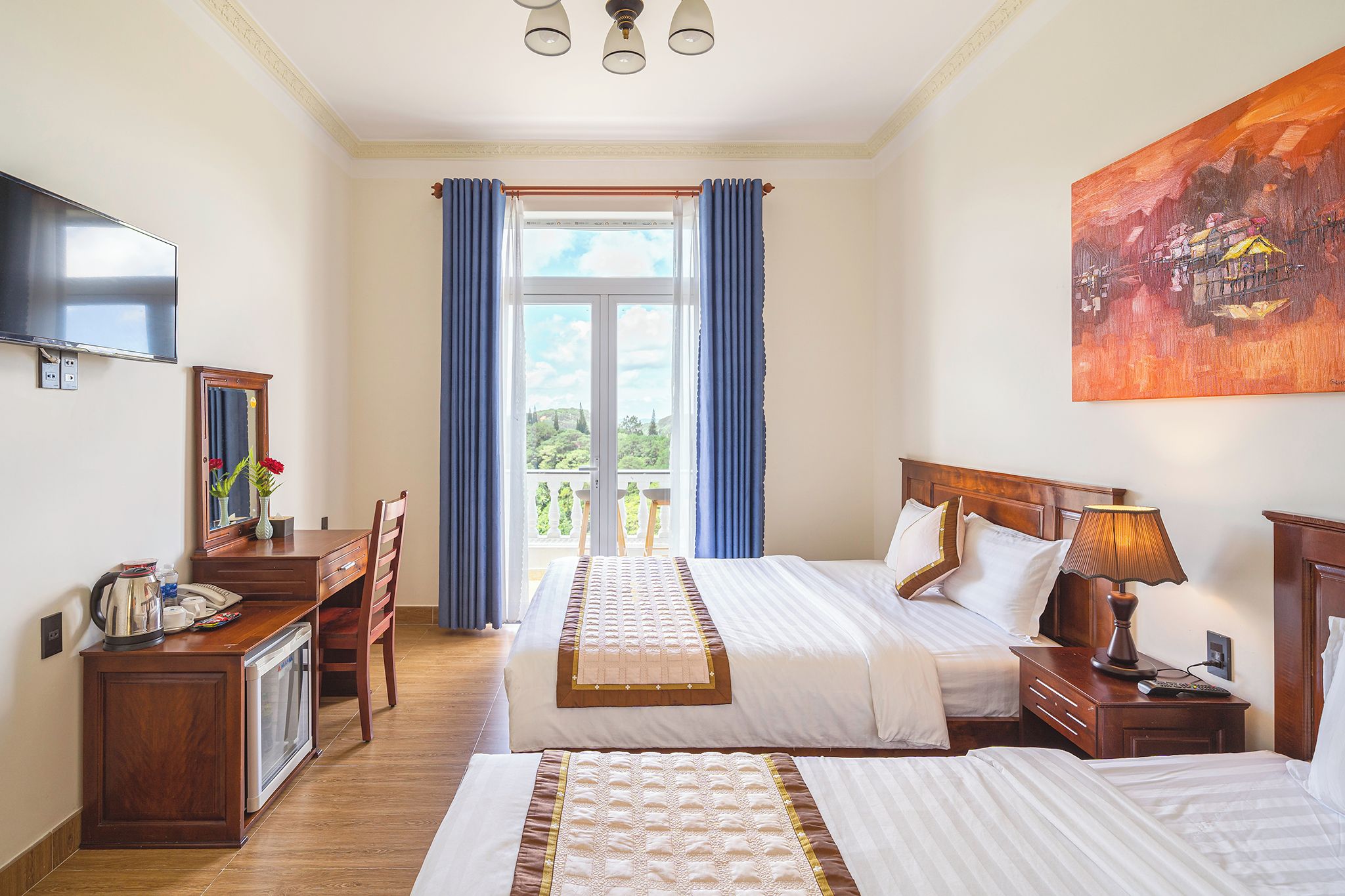 Een hotelkamer met twee bedden, een bureau met telefoon, een koffiezetapparaat en een schilderij aan de muur.