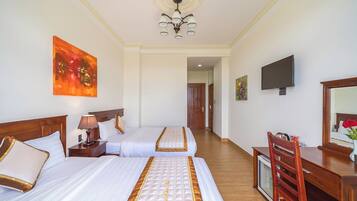 A hotel room with two beds, a desk, a television, and artwork on the walls.