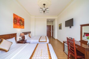 Habitación de hotel con dos camas, un escritorio, un televisor y obras de arte en las paredes.