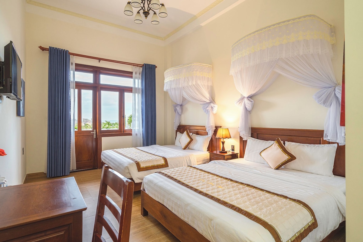 A hotel room with two beds, a desk, a chair, a TV, and a window with curtains.