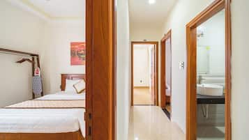 A hotel room with a bed, a wooden wardrobe, a bathroom with a sink, and a hallway leading to another room.