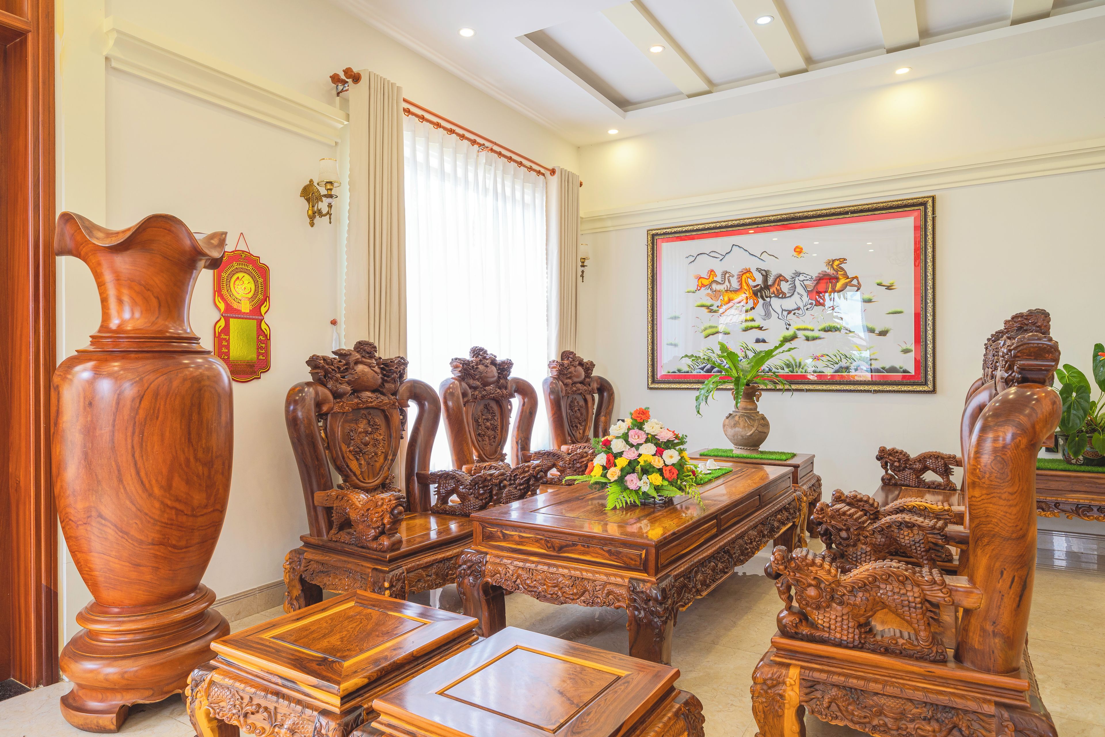 A traditional wooden dining set with intricate carvings, a large vase, and a framed painting on the wall.
