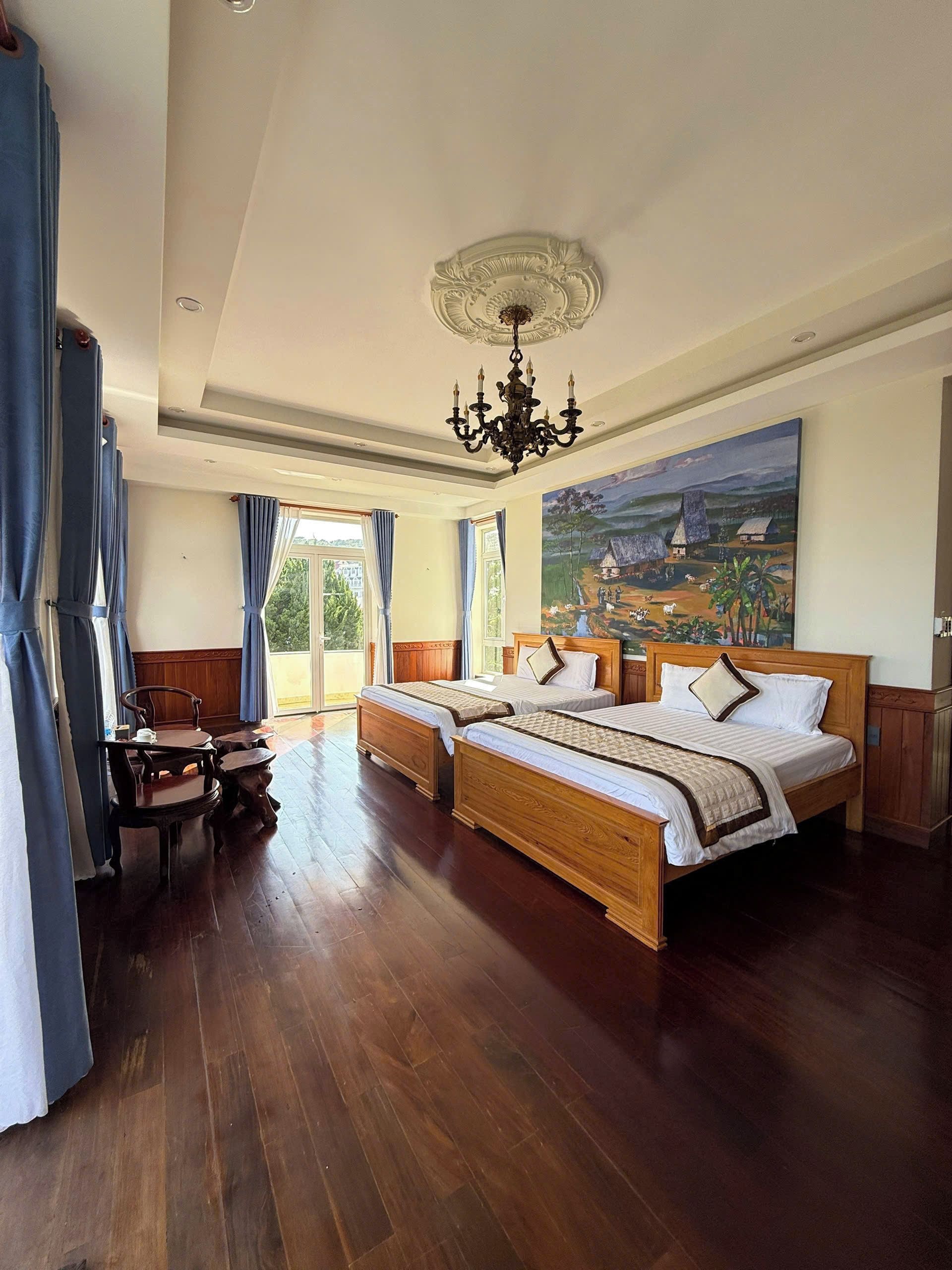 Une chambre spacieuse avec deux lits en bois, un lustre et un tableau au mur.
