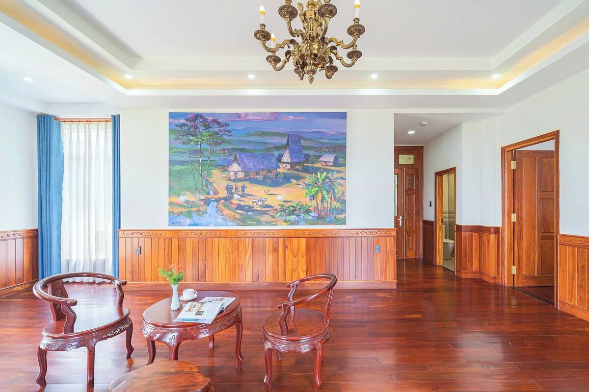 A lobby with wooden paneling, a large landscape painting, a chandelier, and a reception desk.