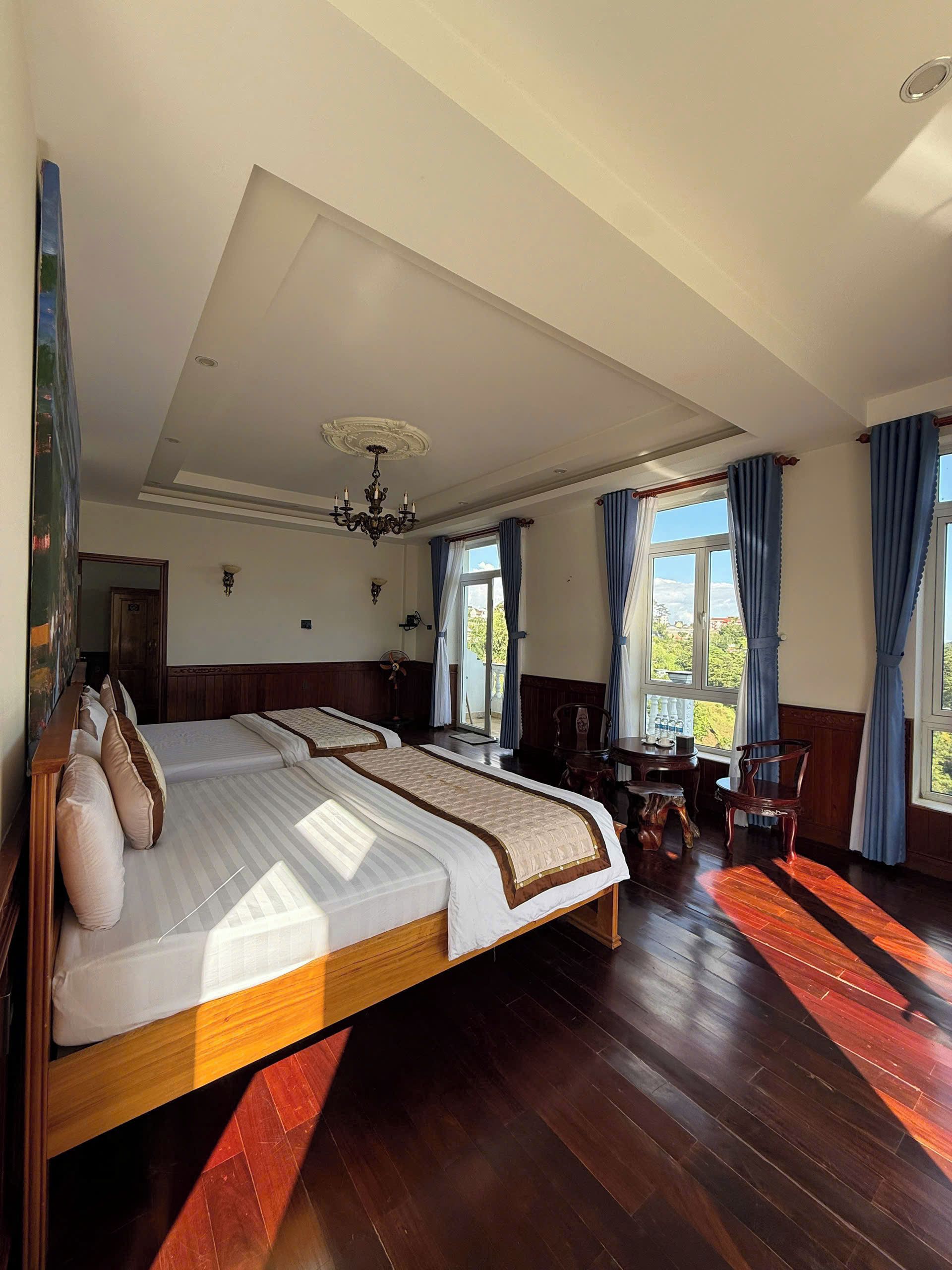 A spacious bedroom with a large bed, a chandelier, and a view of the outdoors through the windows.