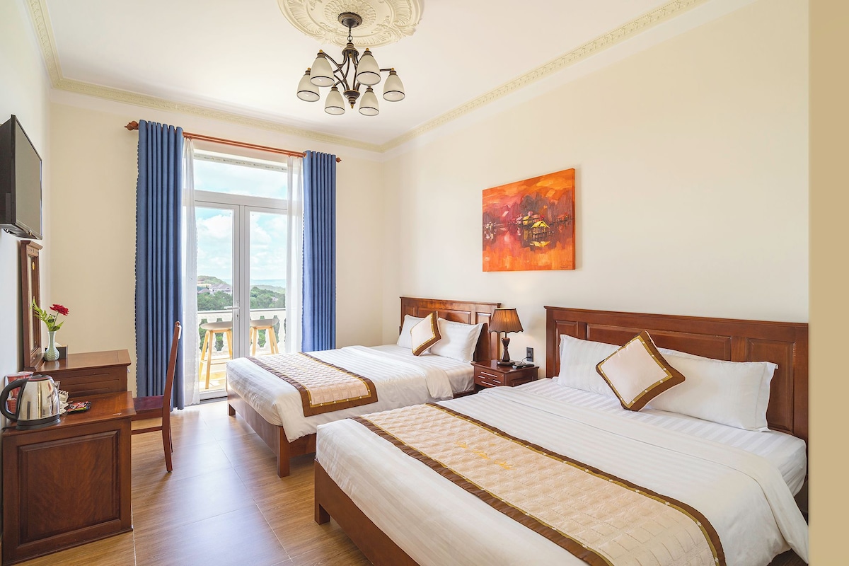 A hotel room with two beds, a television, a desk with a kettle, and a painting on the wall.