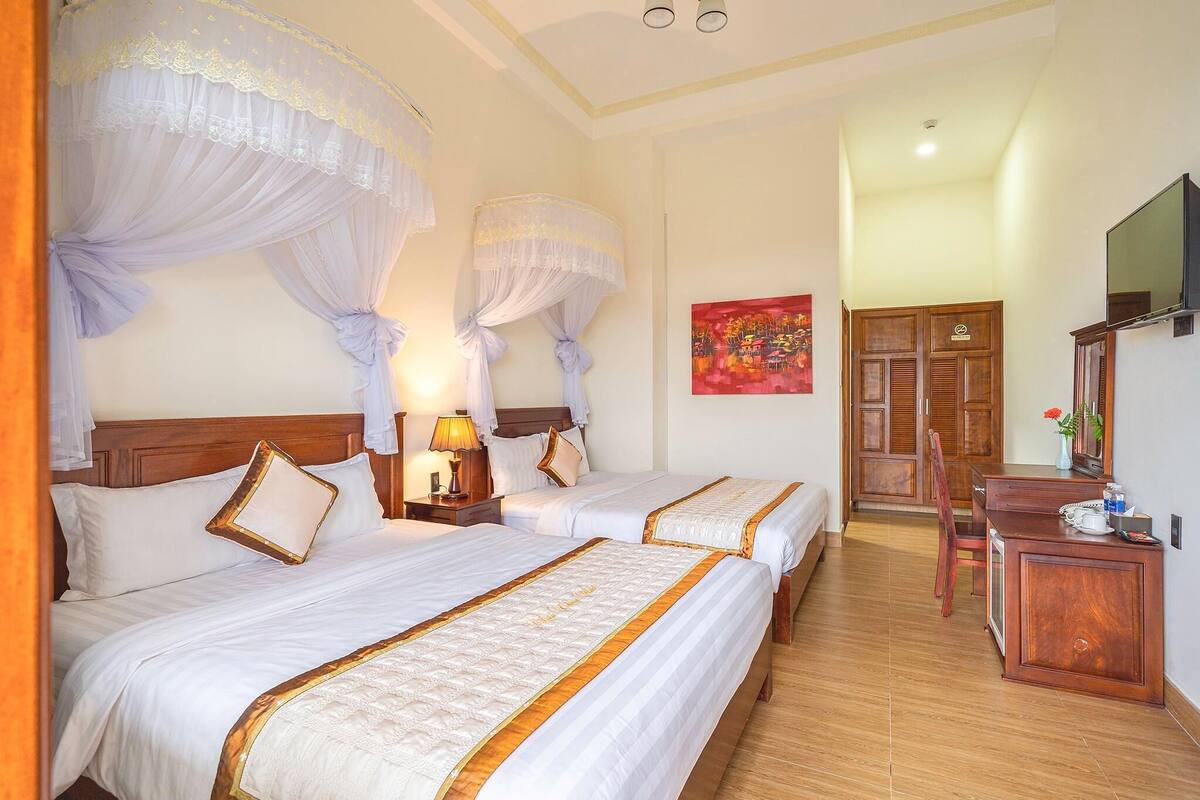 A hotel room with two beds, a wooden desk, a TV, and a painting on the wall.