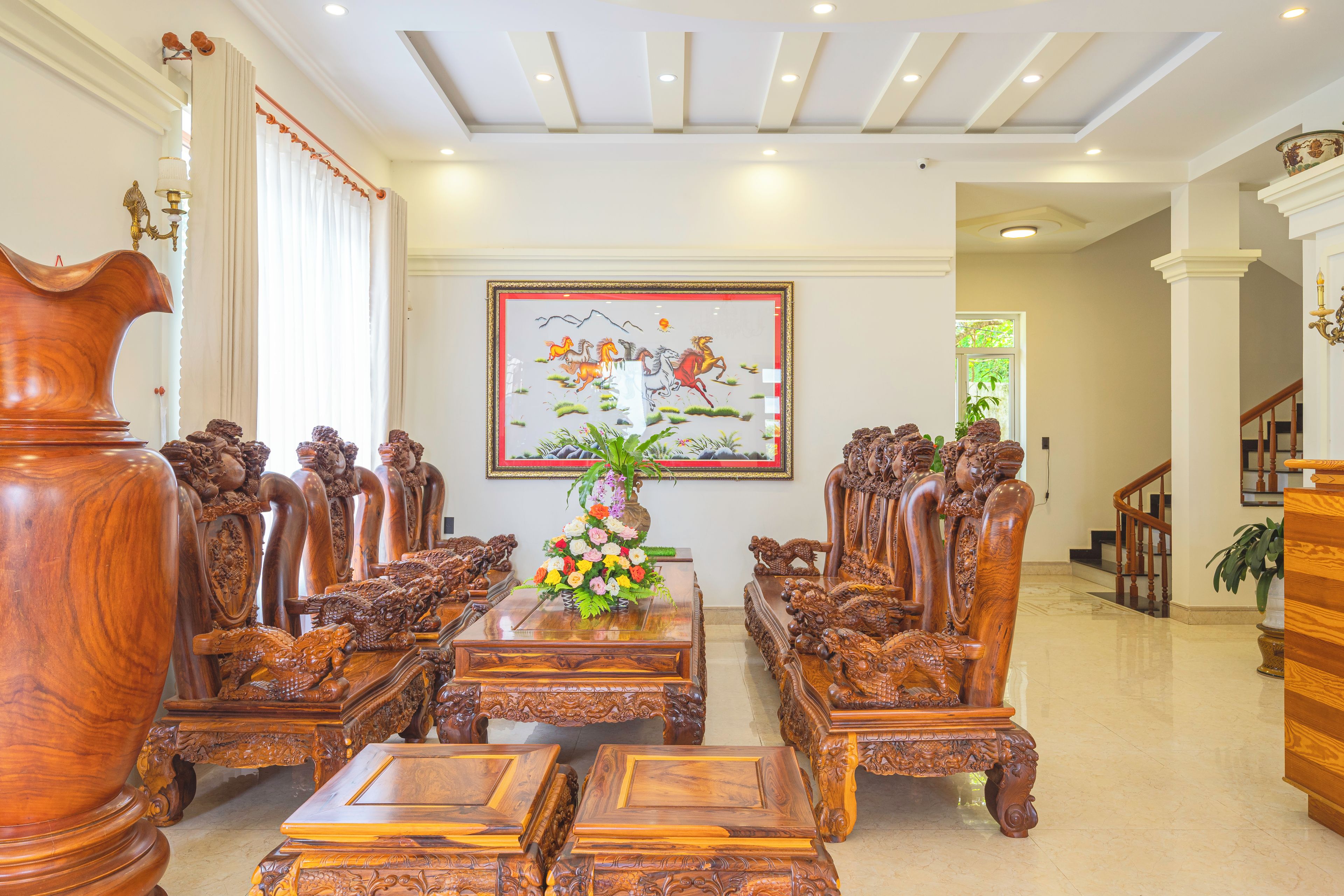A traditional wooden dining room with ornate chairs, a central table with a floral arrangement, and a large framed painting on the wall.