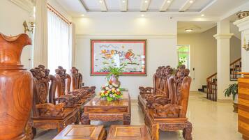 A traditional wooden dining room with ornate chairs, a central table with a floral arrangement, and a large framed painting on the wall.