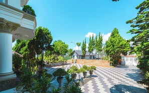 A courtyard with a checkered floor, surrounded by potted plants and trees, leading to a building with a tiled roof. - Dieu Thong Hotel (Xuan Huong - Da Lat)