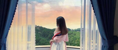 A person standing on a balcony with a view of a green landscape and a cloudy sky.