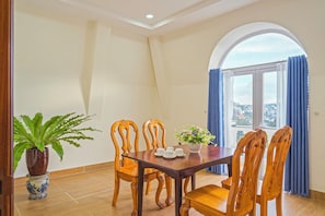 A dining area with a wooden table and chairs, a potted plant, and a view through a window with curtains. - Dieu Thong Hotel (Xuan Huong - Da Lat)