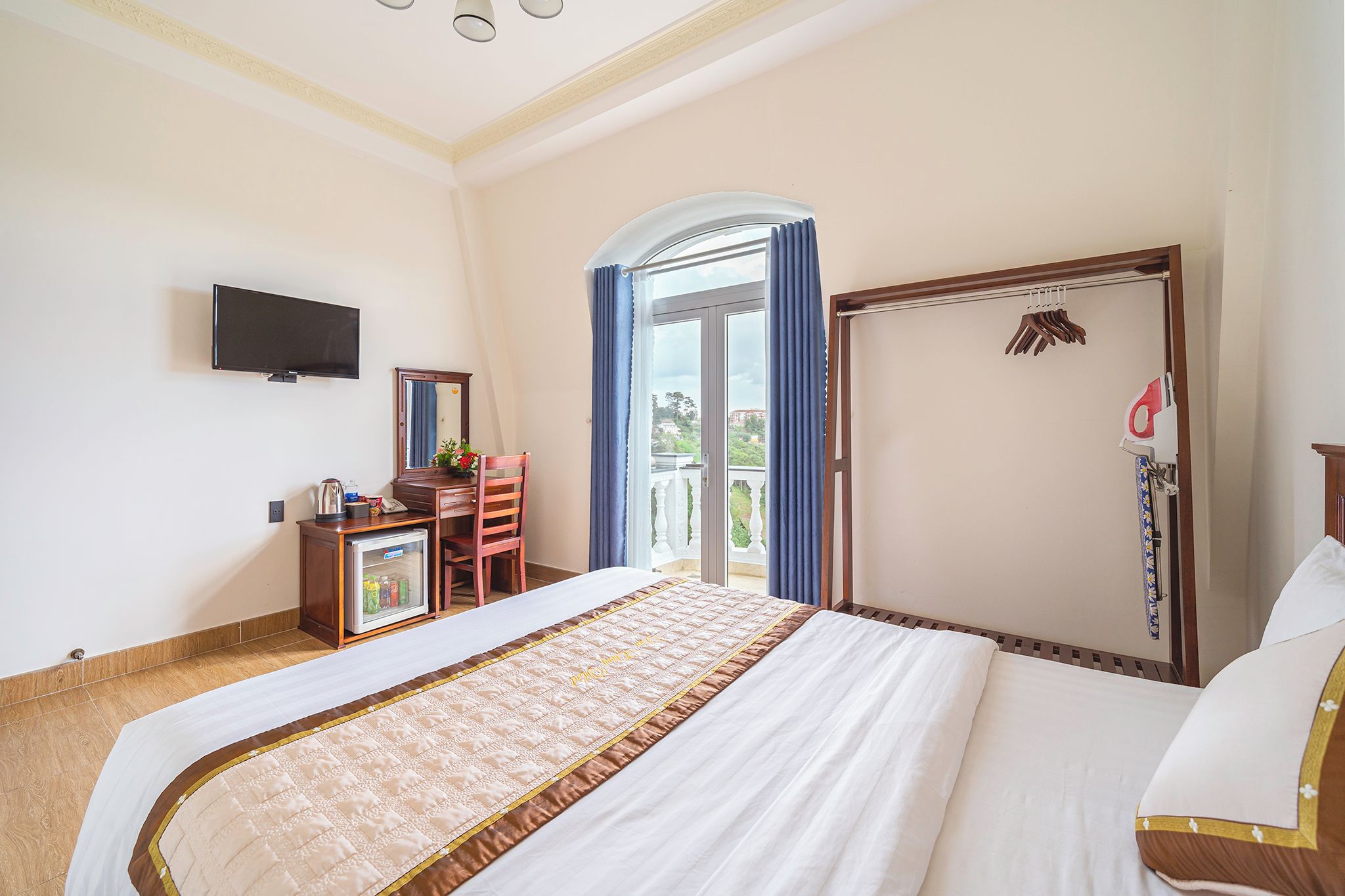 A hotel room with a bed, a desk with a mirror, a television, and a view of the outdoors.