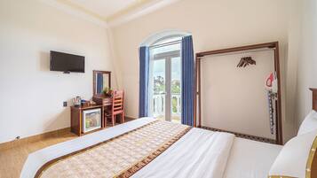 A hotel room with a bed, a desk with a mirror, a television, and a view of the outdoors.