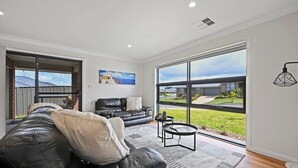 Un salon moderne avec un canapé en cuir noir, une table basse et une grande fenêtre donnant sur un quartier résidentiel.