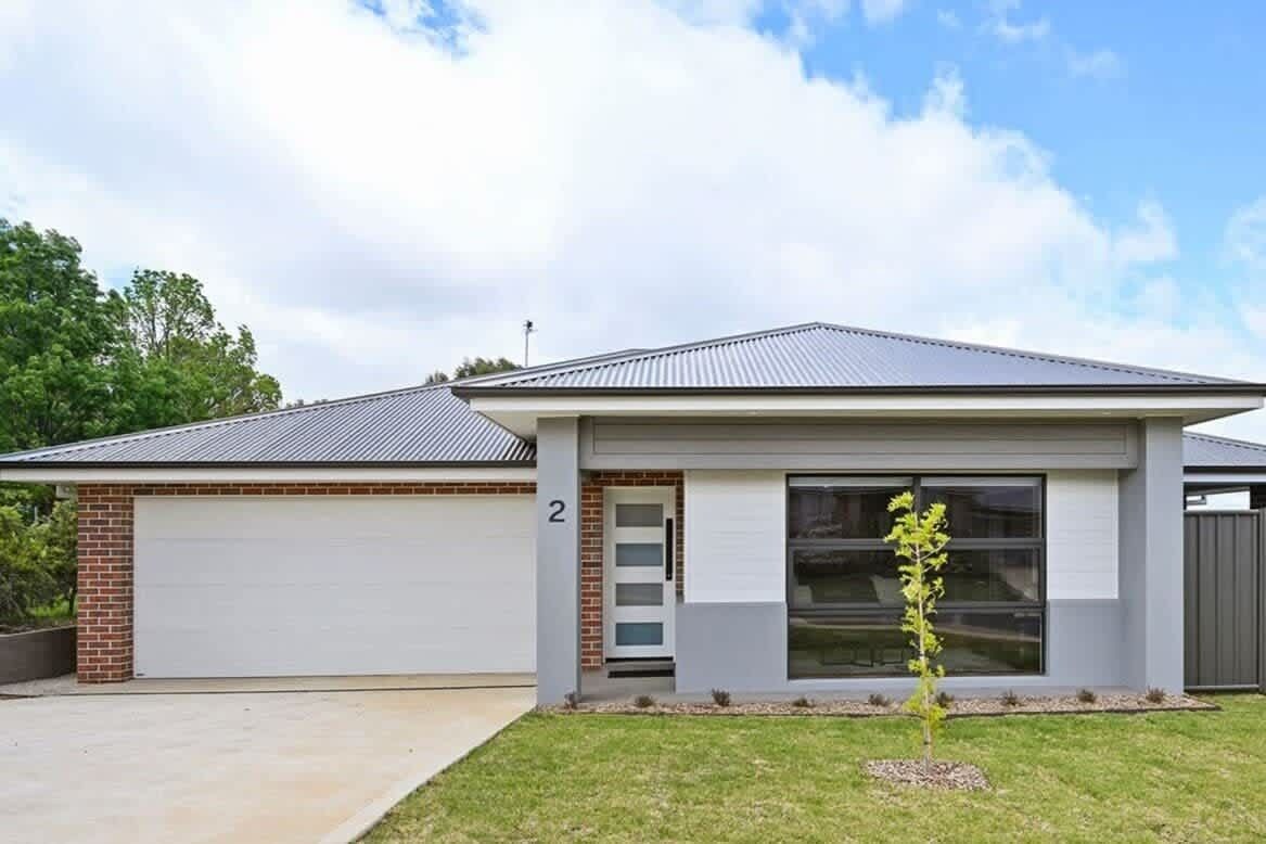 A modern two-story house with a garage, a small front yard, and a clear sky.