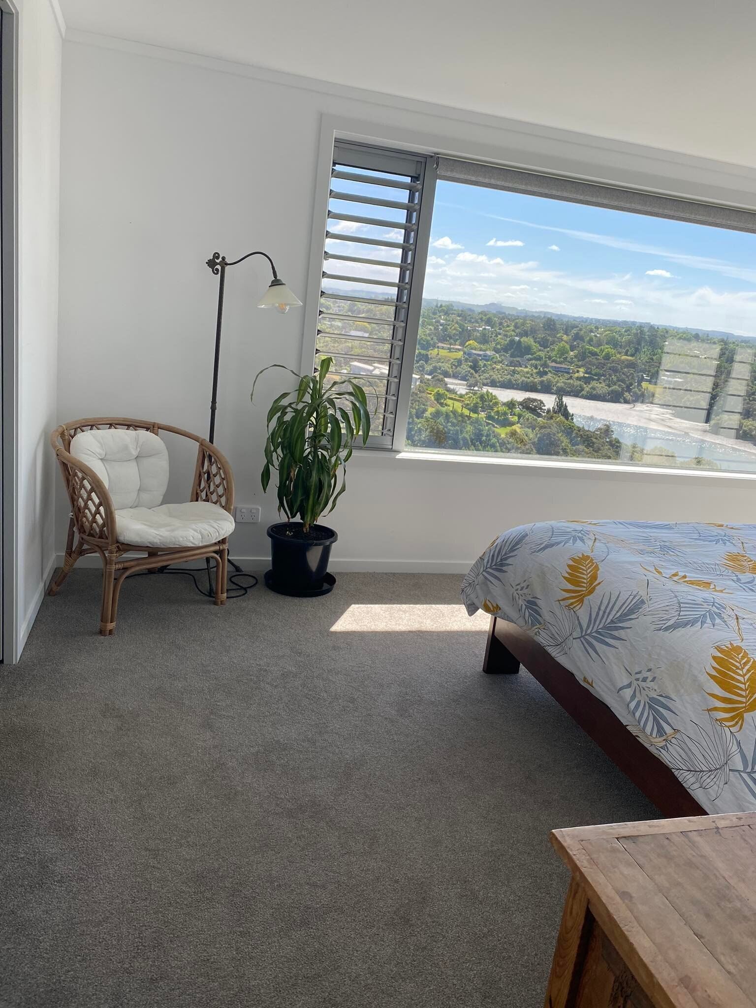 Ein Schlafzimmer mit großem Fenster, einem Sessel, einem Blumentopf und einem Bett mit floralem Überwurf.