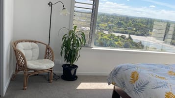 Ein Schlafzimmer mit großem Fenster, einem Sessel, einem Blumentopf und einem Bett mit floralem Überwurf.