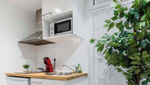 Une cuisine compacte avec des meubles blancs, un four à micro-ondes, un petit évier, une poubelle et une plante en pot.